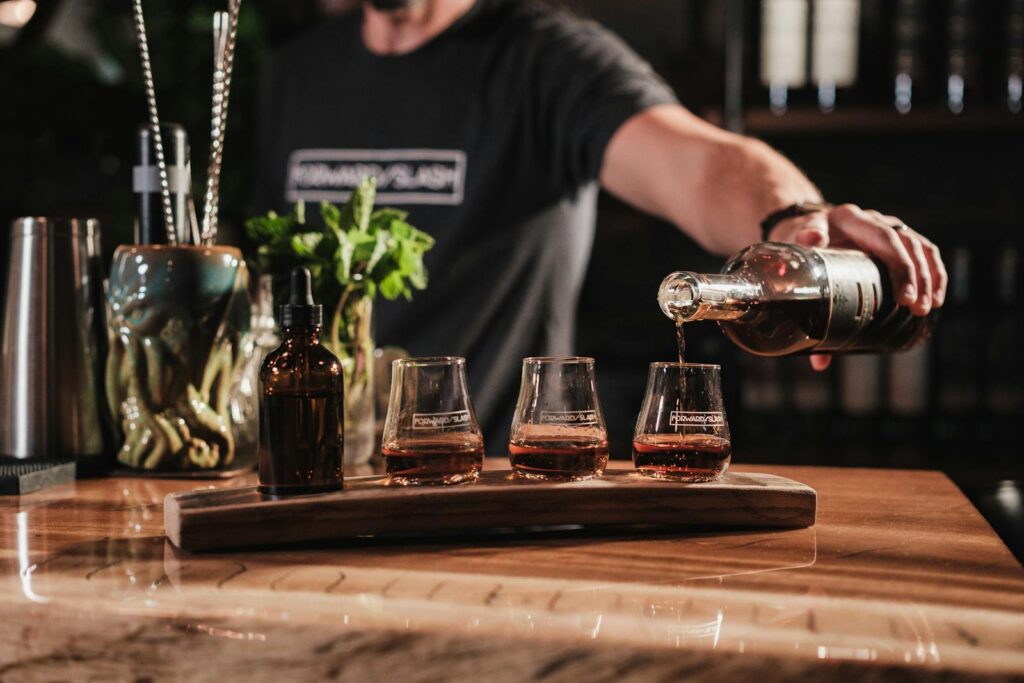 Bartender pouring whiskey into glasses at a bar with cocktail setups in view.