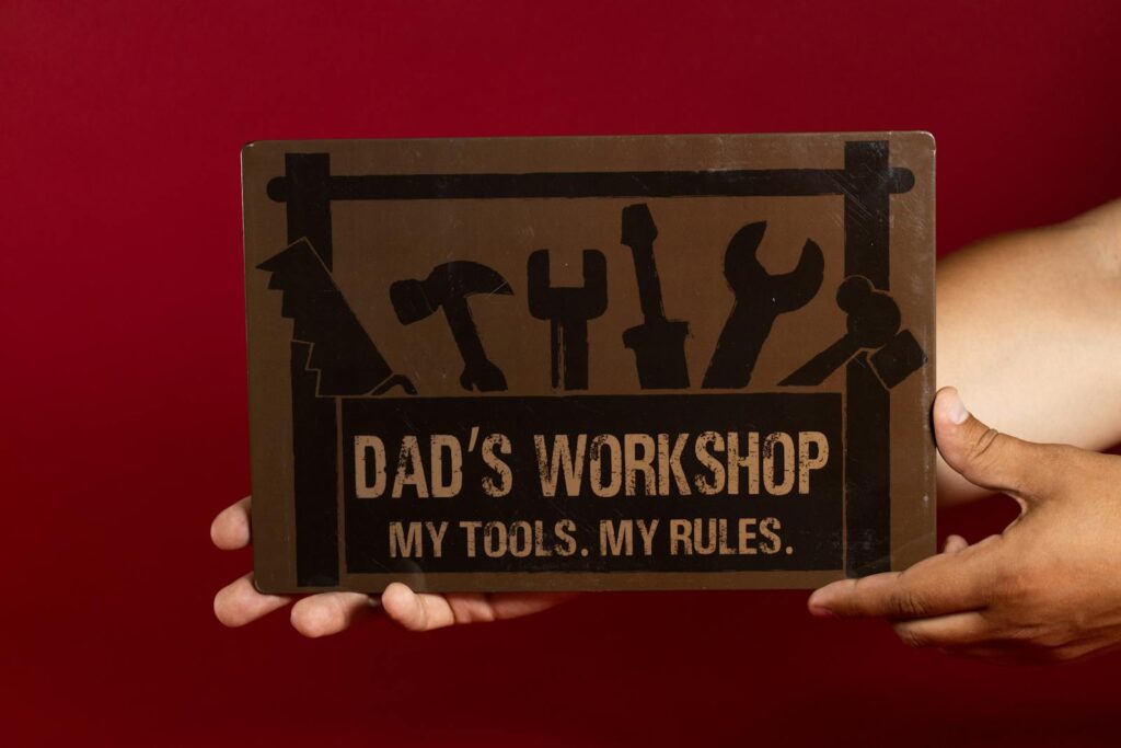 A hand holds a sign with 'Dad's Workshop' text, ideal for Father's Day.