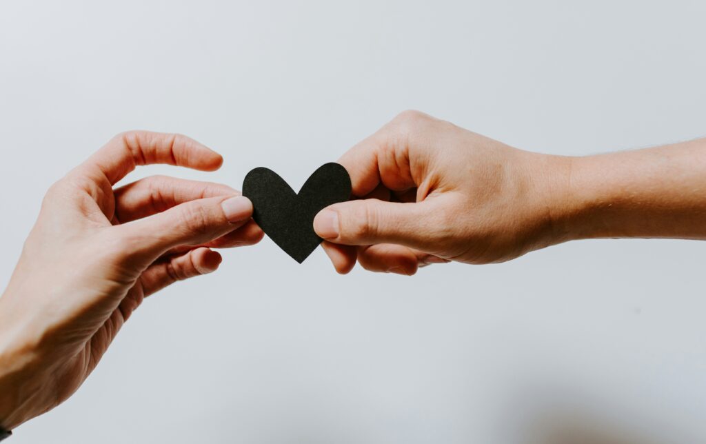 two hands passing a paper heart to support a grieving friend